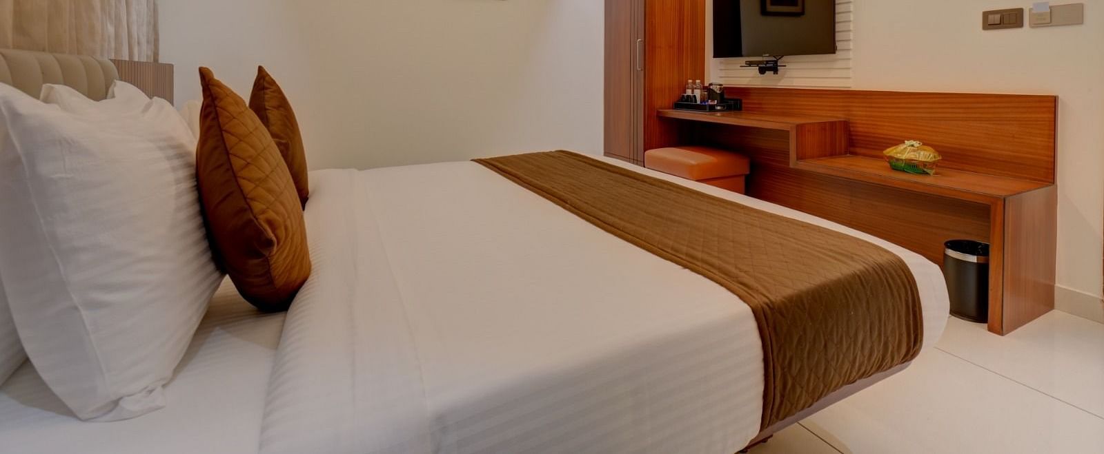 An image of a room featuring a bed with a wooden table in front, and a television mounted above it at Hari Govindas, Siddappa Square.