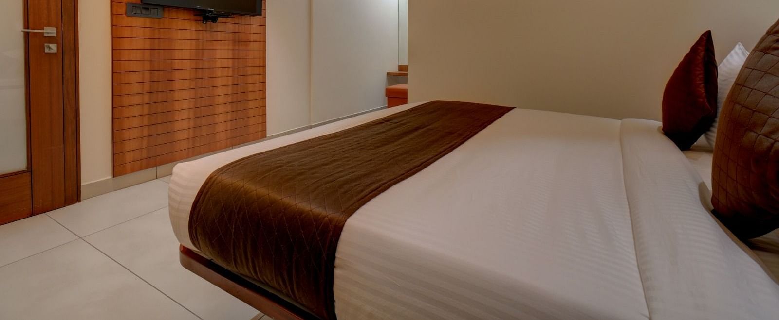 Side view of a room with a bed and a television in front of it at Hari Govindas, Siddapa Square.