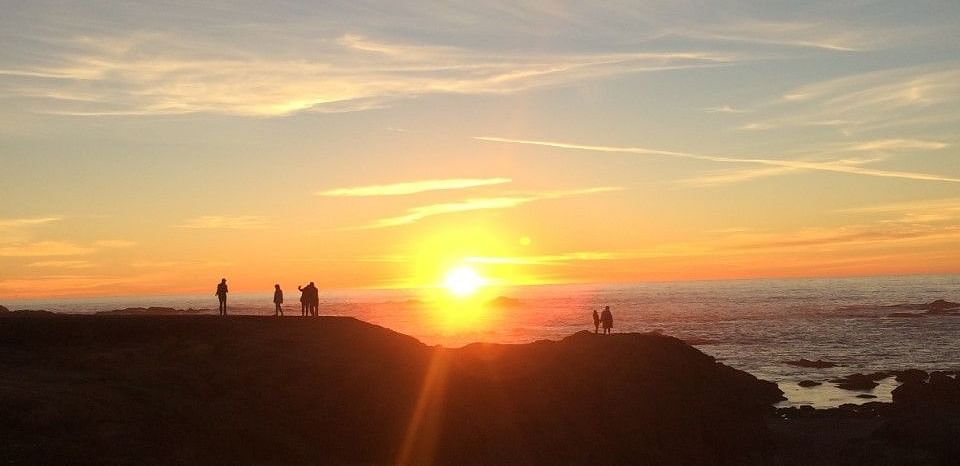 A sunset over the ocean with silhouettes of people on a hilltop.