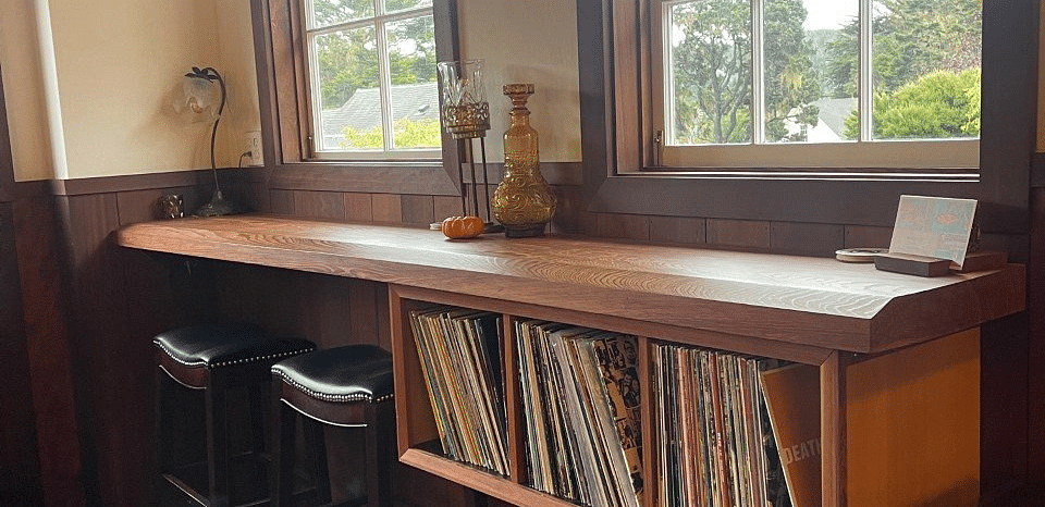 Interior of a room with a long wooden counter, stools, and two windows.