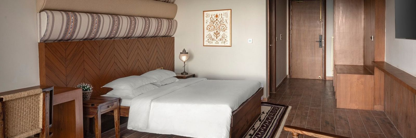An elegantly designed room with patterned fabric wall decor above the bed, wooden furniture, and a comfortable seating area - The Samai, Bhimtal