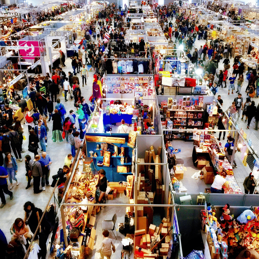 An aerial view of a toys convention with numerous stand and people walking in and out to buy or browse the selections.
