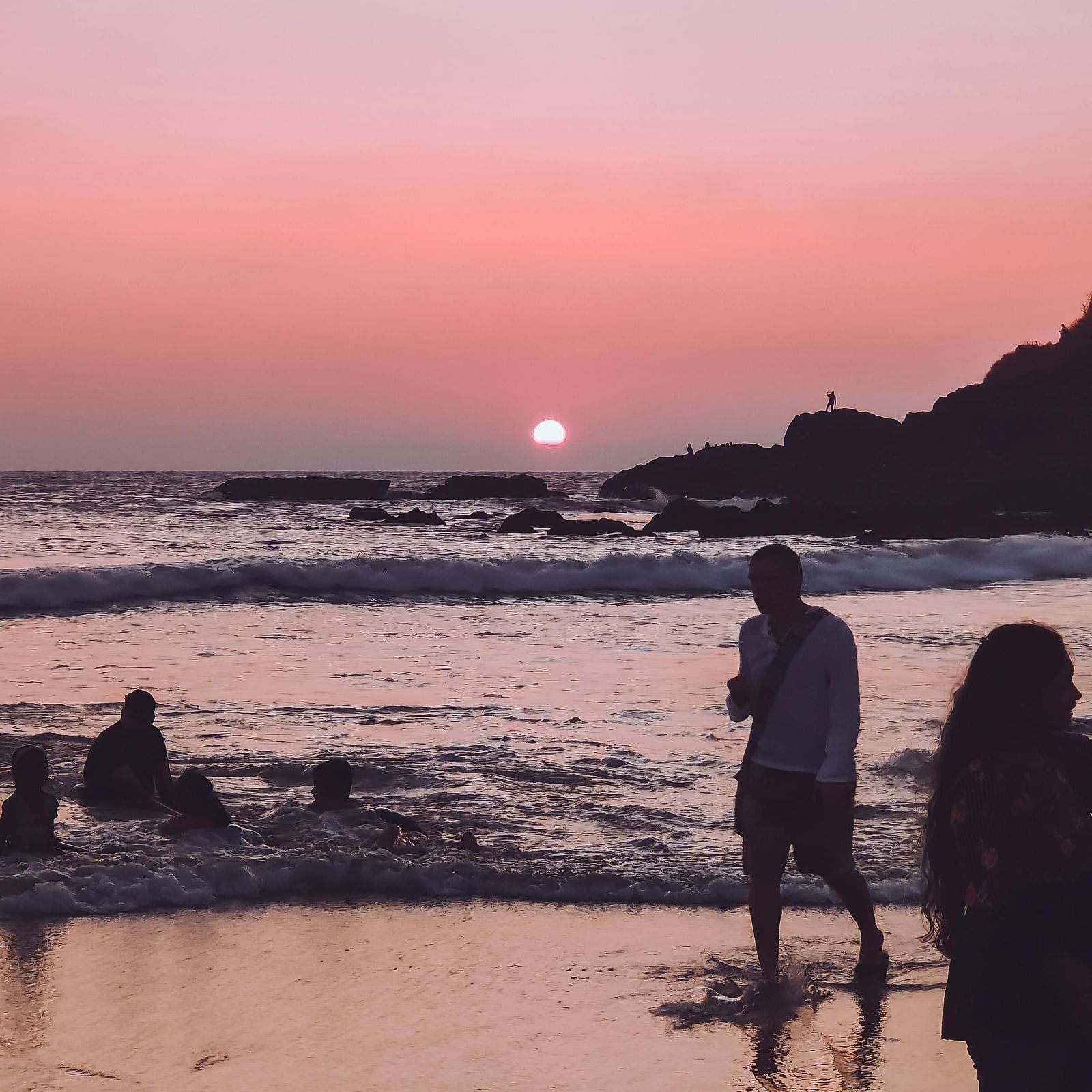 A scenic view of the sunset at Baga Beach with people walking around.