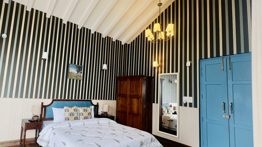 Bedroom at Faraway Cottages, Auli, with high ceiling, striped accent wall, double bed, wooden furniture, and wardrobe.