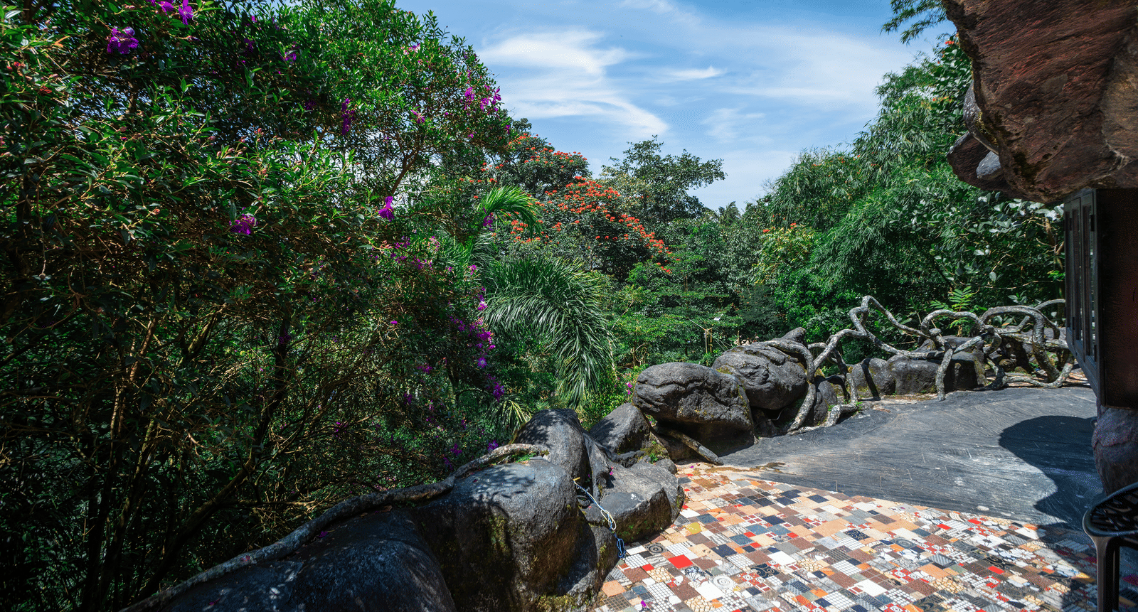 An exterior view of the Cave Room area at Parakkat Nature Hotel and Resorts, Munnar, featuring natural rock formations, and a clear sky above the dense foliage.