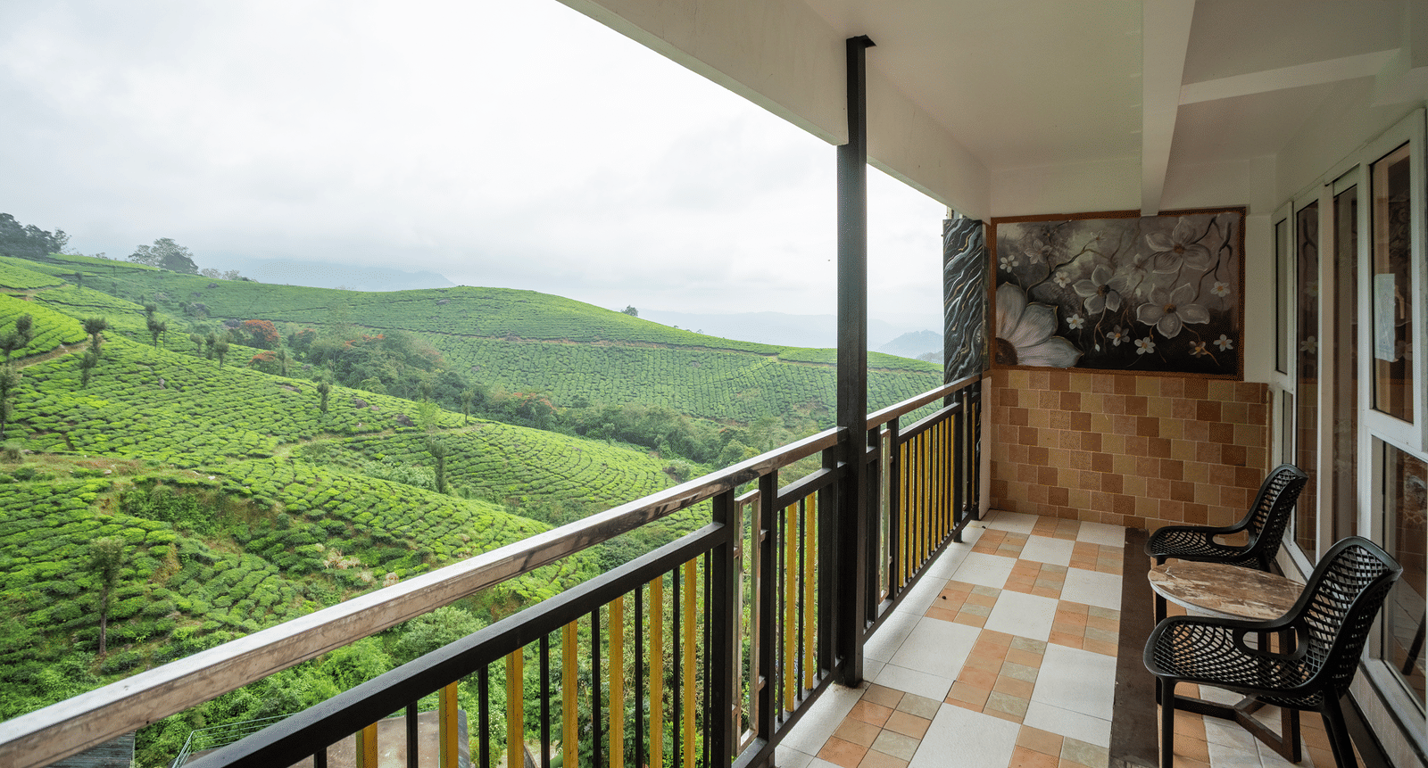 The private balcony of the Honey Moon Suite at Parakkat Nature Hotel and Resorts, Munnar, featuring a protective railing, patterned floor tiling, and a wide view of the expansive terraced hills.