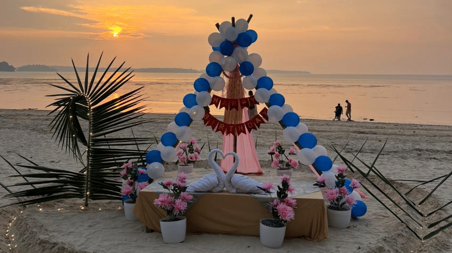 A beachside teepee decorated with balloons and a seating setup, with a Happy Birthday sign displayed at the top and people visible near the shoreline in the background at Silver Sand Sea Princess Beach Resort, Port Blair