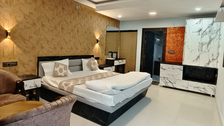 A modern bedroom with a large bed, patterned tan wall panelling behind the headboard, and dark wood furniture on a polished light-coloured floor | Nandan Resort