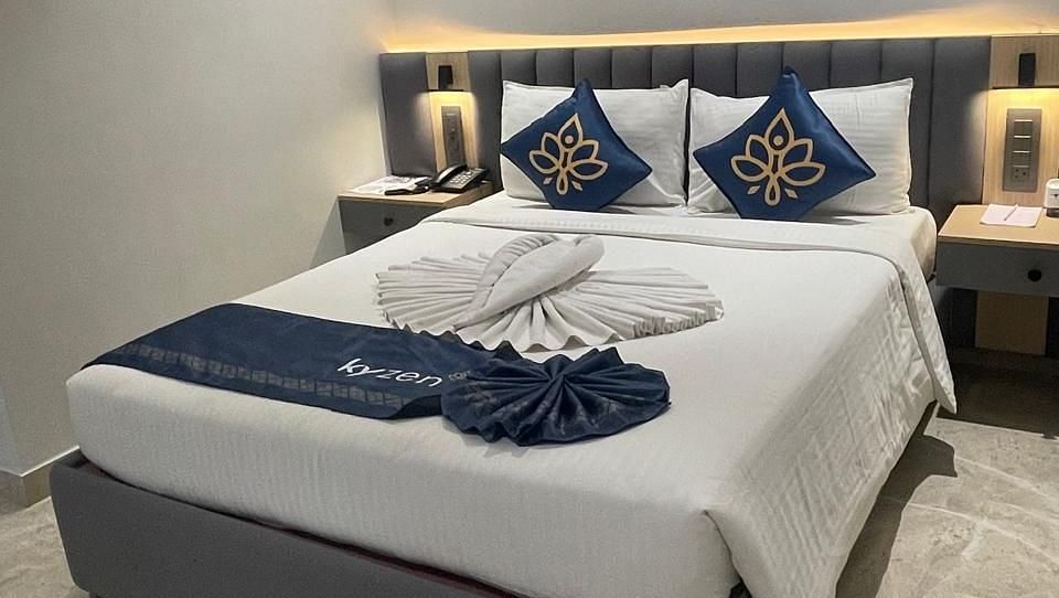 Brightly lit bedroom with a plush bed and decorative pillows at Hotel Kyzen HiTech City – Your Zenly Stay
