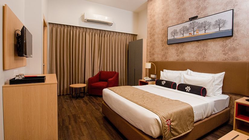 a plush bed with warm toned interiors and room amenities - Mastiff Hotel, Ankleshwar