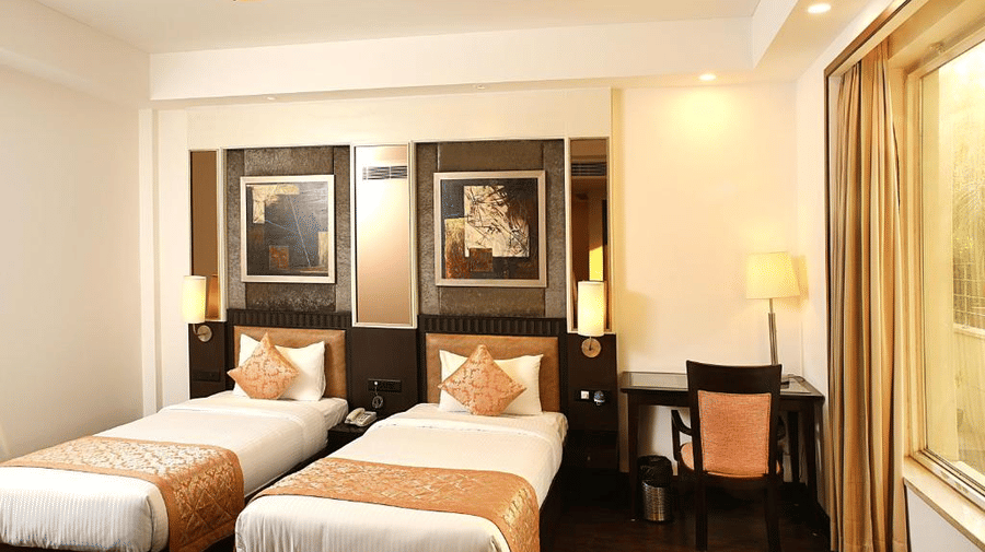 2 single beds with orange accents sit neatly in a room at Eastlynn Collections Huda City Centre, Gurugram.