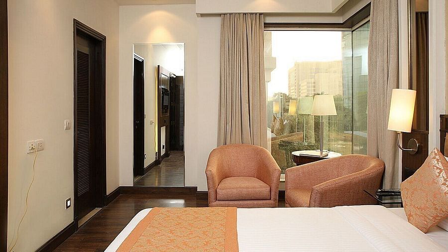 Executive Room with a double bed, bedside table with a lamp on top, cushioned seating with a table in front, and a window behind at Inde Signature Tower, Gurgaon