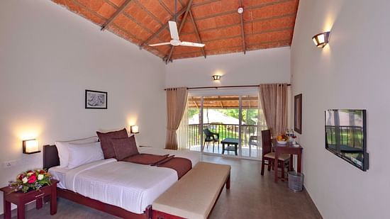 A bedroom with a view of a balcony overlooks trees, offering a tranquil setting. - Abad Brookside Lakkidi, Wayanad