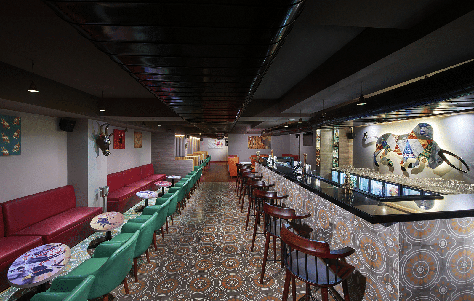 A brightly lit bar with red couches, a long bar counter, and a colorful wall mural | Regency Tirunelveli By GRT Hotels