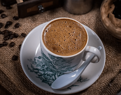 A cup with a drink, a spoon kept beside the cup. 