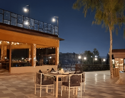 An outdoor dining area at night with a table and chairs set on a paved patio.- Bamboo Saa Resort & Spa, Udaipur