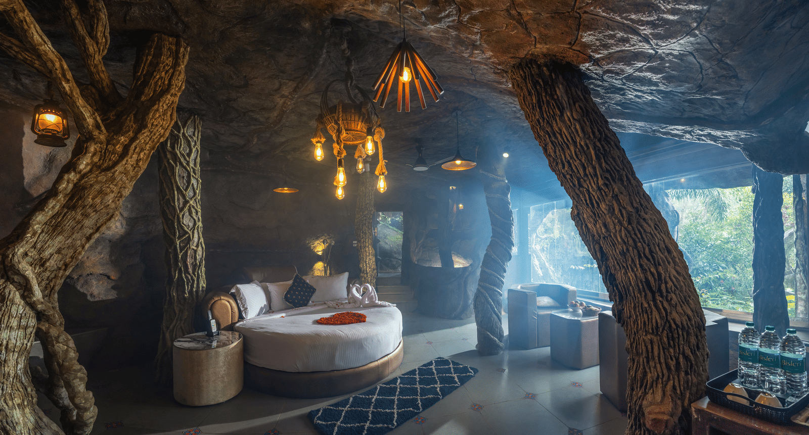 The sleeping area in the Cave Room at Parakkat Nature Hotel and Resorts, Munnar, featuring a circular bed, soft lighting, and carved stone accents on the walls and ceiling.