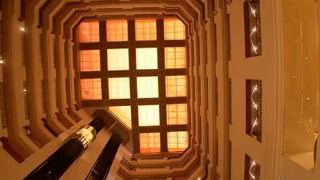 Interior view of a hotel featuring corridors illuminated by warm yellow lights, captured from an upward angle.