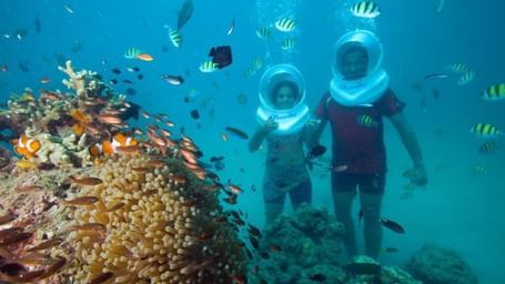 Two people sea walking among tropical fish and coral.
