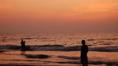 an image of a beach where two people are enjoying the waves during the sunset