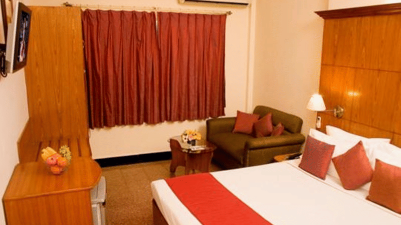 An Executive Room at Ramanashree California Resort with a bed, wooden furnishings, air conditioning, TV unit, seating area with sofa, and warm, inviting interiors.