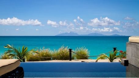  A luxurious infinity pool seamlessly blends with the turquoise ocean under a blue sky - Tamarind Hills Resort and Villas - Antigua