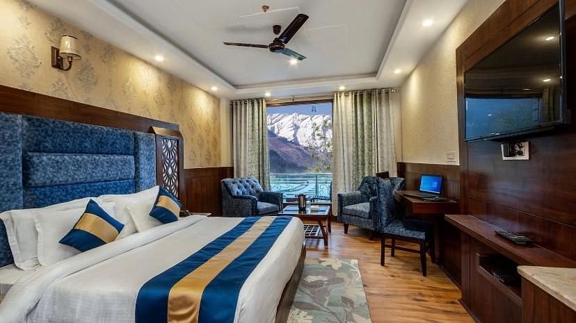  A spacious hotel room with a comfortable bed, a seating area, and a view of mountains | DLS La Serene Manali