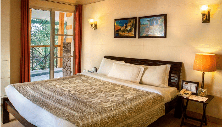 Deluxe room designed with aesthetic interior with  beautiful shades of brown while showcasing a beautiful balcony beside the bed - Lamrin Norwood Green, Palampur
