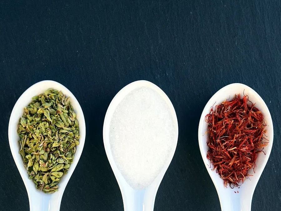 Three white spoons filled with different spices – green, white, and red – against a dark background.