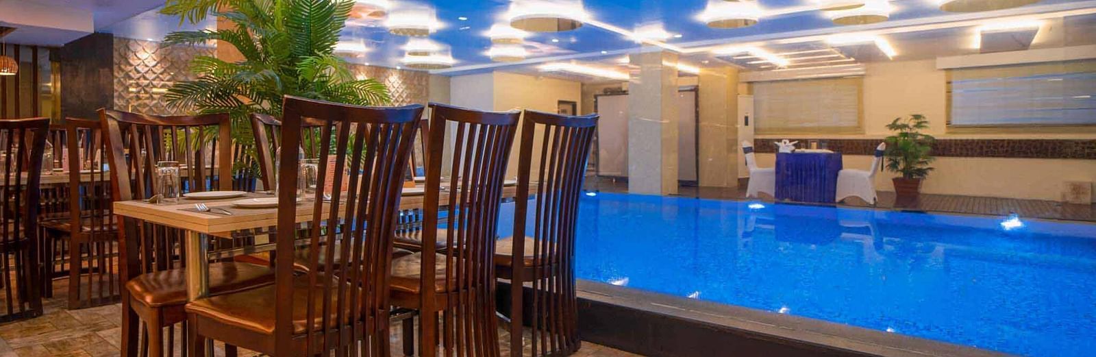 A dining area at Mansha Hotel Regency with a distinctive blue-lit ceiling, dark wooden tables and chairs, and a pool in the foreground.