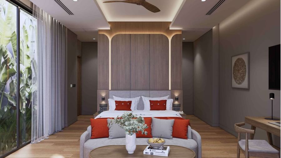A room with a king size bed, red and grey cushions, wooden furniture, sofa with coffee table, and full-length windows opening to garden views at Ramada Resort by Wyndham Khao Lak.
