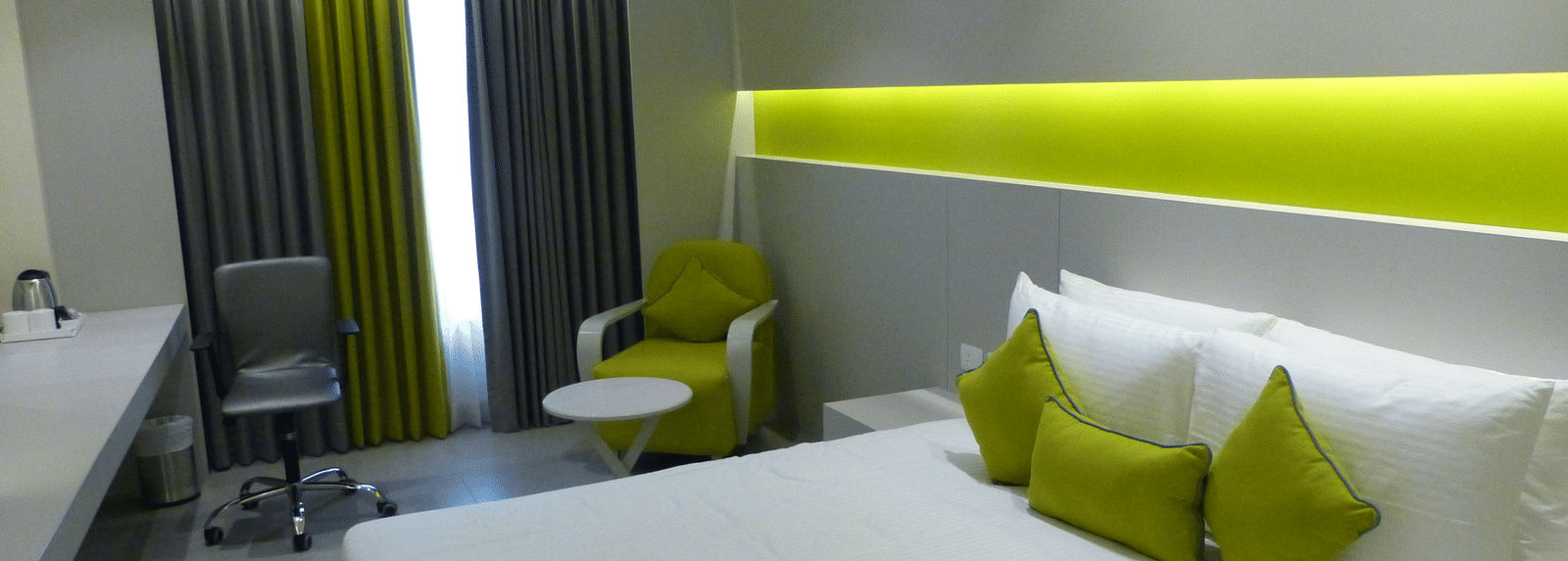  Spacious twin beds with headboards line the wall, large windows with curtains cover them, and a sofa is placed near the window