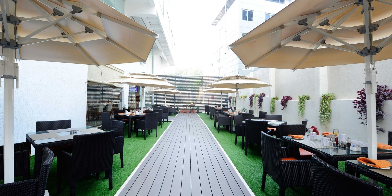 Coffee Shop at The Cunningham Hotel featuring outdoor dining space with black wicker furniture, green flooring, large umbrellas, and elegant table settings featuring orange napkins
