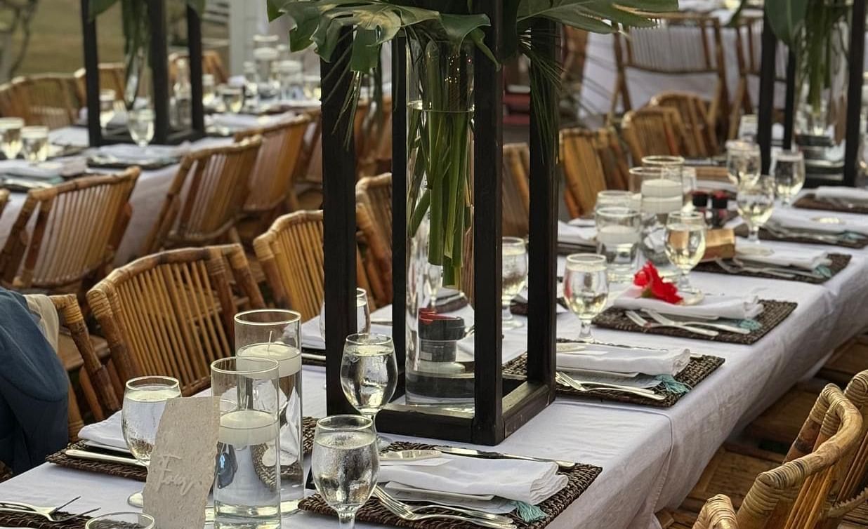 A huge open dining area meant for wedding guests. There are chairs placed with dining tables which features plates, towels, table mat, cutlery, etc. along with flower vases.