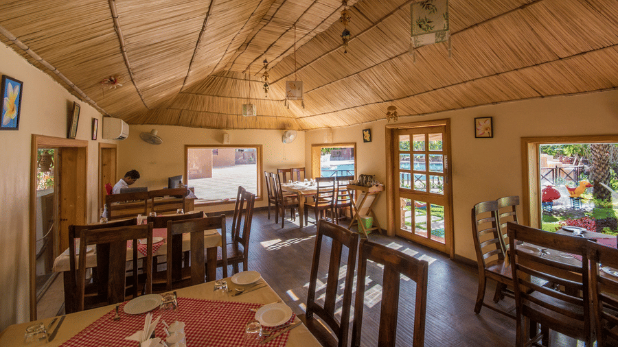 A dining room interior with multiple tables and chairs arranged under a sloped wooden panel ceiling at Garh Govind.