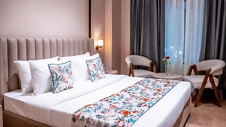 Bedroom with a queen size bed with chairs and window with a curtain in the background at ASTER GRAND BY ZENQ SAKET.