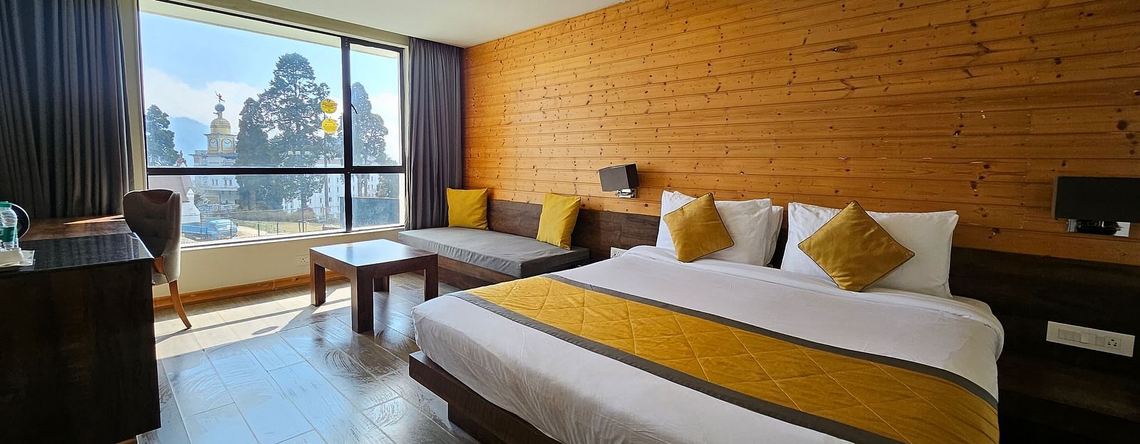 An image of a deluxe room with a bed, a couch, a table, work desk, chair, and an expansive window overlooking the view - Yashshree Sanderling, Darjeeling