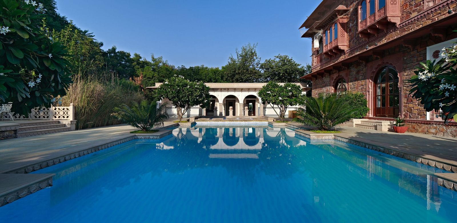 Shot of a large, clear blue swimming pool with a building and some trees in the background - Khas Bagh, Jaipur