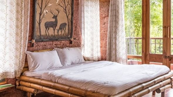 A bedroom with a wooden bed frame, tan walls, and a window with patterned curtains.
