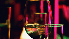 Wine glass and tumblers on a bar, illuminated by vibrant lights, creating a lively atmosphere.