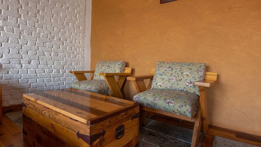 Wooden chairs with floral cushions and a chest table against a white brick wall. - Blusalzz Homes The Himalayan Bungalow, Almora