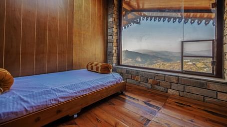 A cosy room with wooden walls, a single bed, and a large window showcasing mountain views. - Blusalzz Homes The Himalayan Bungalow, Almora