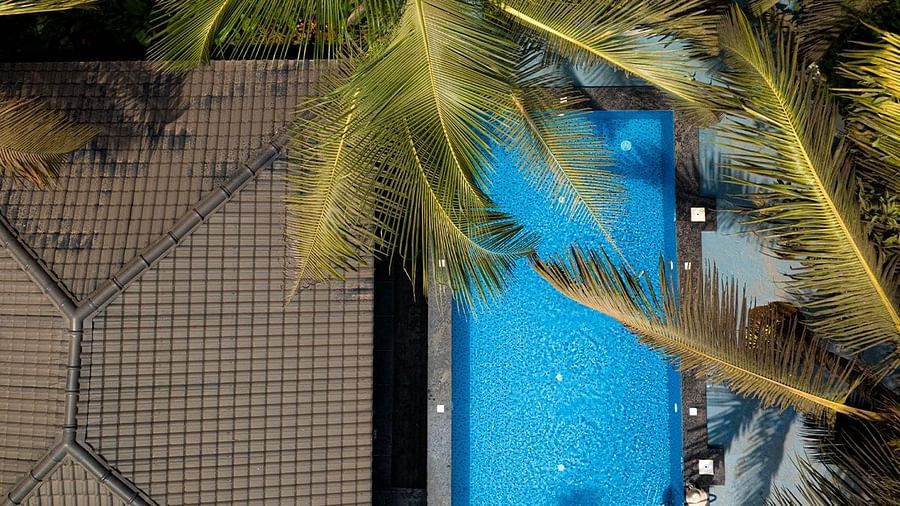 A view from above, looking down at a bright blue swimming pool surrounded by greenery and the side of Kssemya.