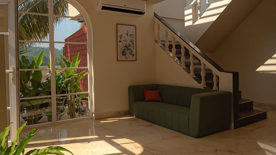 An interior view looking up a curved staircase with wooden treads and a white balustrade. Sunlight streams in from above, illuminating a seating area with a dark sofa and plants on the ground floor at Kssemya