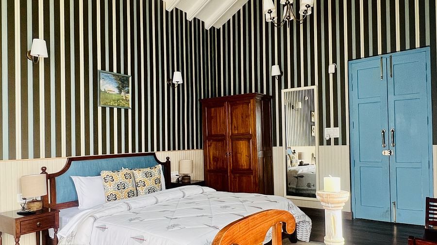 Elegant bedroom with striped wallpaper, wooden flooring, and a traditional wooden bed decorated with colorful cushions in a boutique hotel | Faraway Cottages, Auli