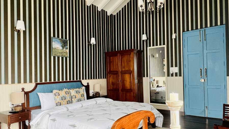 Interior of a bedroom featuring bold black-and-white striped wallpaper, a white vaulted ceiling, a large bed with patterned cushions, and bright blue double doors at Faraway Cottages.