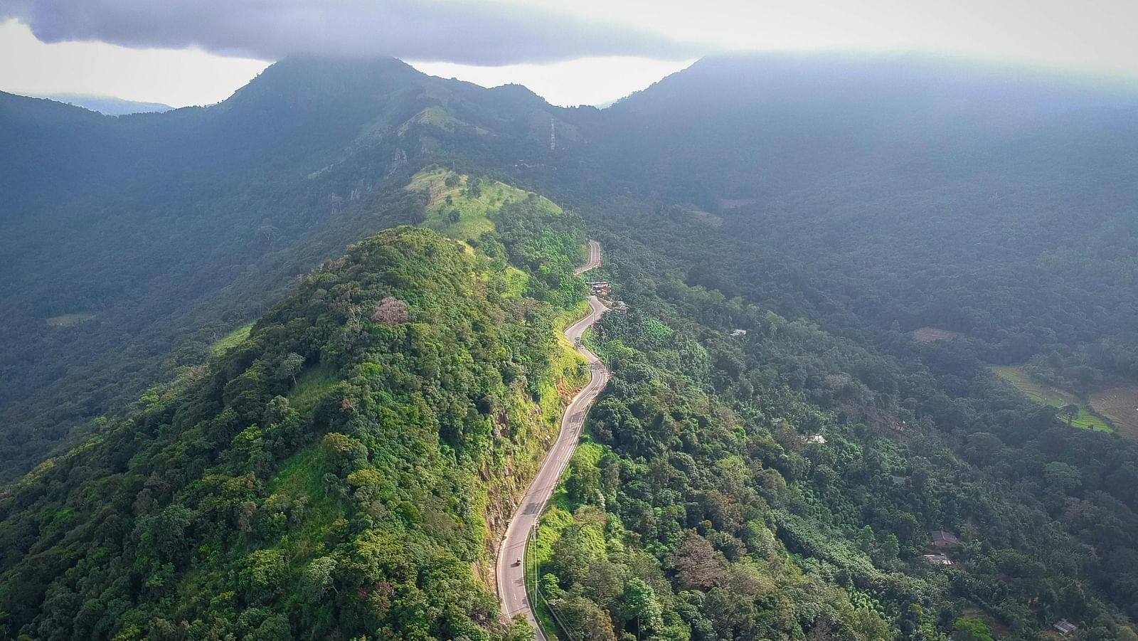 A stunning aerial view of a narrow road cutting through lush green mountains.