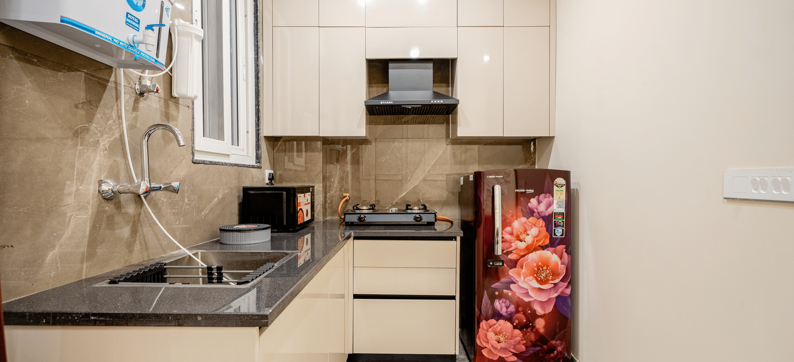 Modern compact kitchen with cabinets, sink, microwave, gas stove, and floral fridge at Lime Tree 1BHK Service Apartment Near Artemis Hospital Gurgaon.
