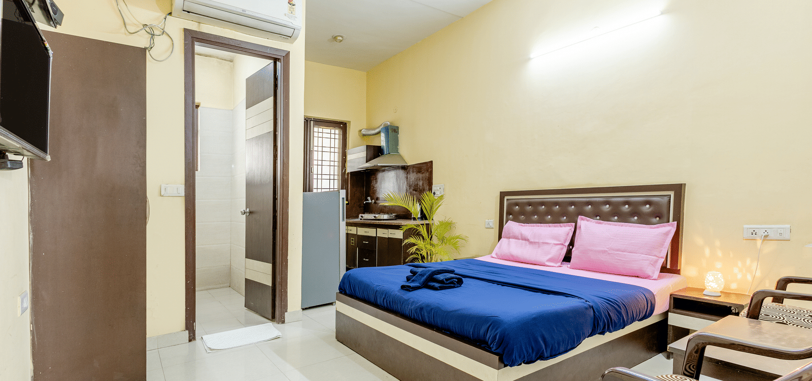 An image of a bedroom featuring a king size bed, a wardrobe, a bedside table, a seating area with chairs and tables,  and a small kitchenette - Lime Tree Studio Serviced Apartment, Gurgaon