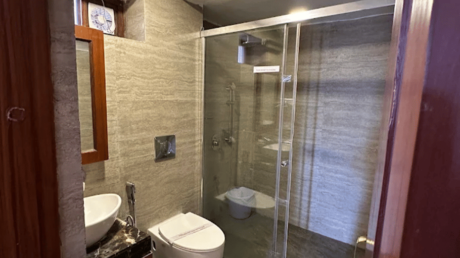  Hotel Devnadi, Haridwar | A bathroom with a toilet seat, a sink, a mirror, and lights.
